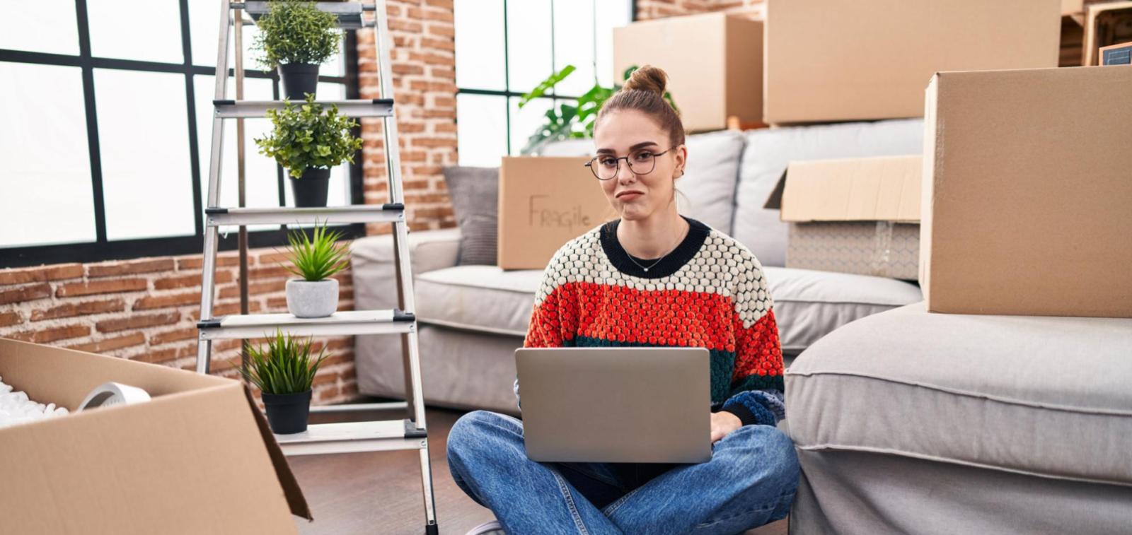 A person sat on the floor of their home after moving in, surrounded by moving boxes.